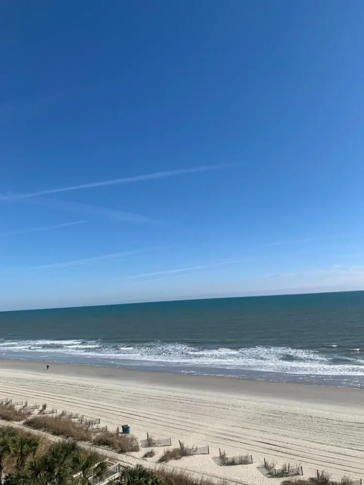 A wide view of a beach with a sandy shore and ocean waves under a blue sky.